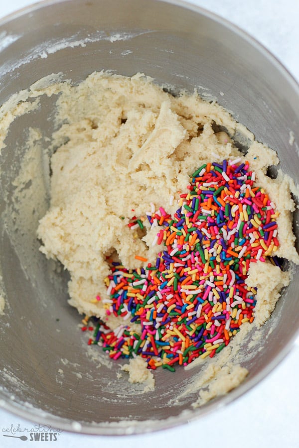 Sugar cookie dough in a stainless bowl topped with sprinkles.