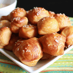 Pile of soft pretzel bites on a white plate sitting on a green striped towel.