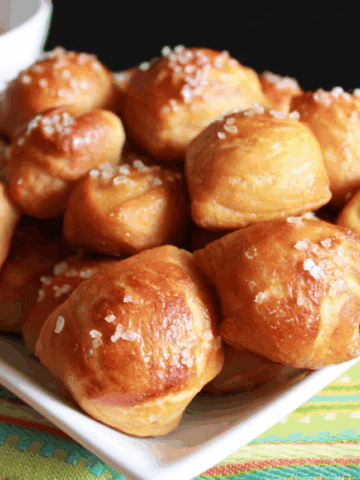Pile of soft pretzel bites on a white plate sitting on a green striped towel.