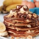 Stack of pancakes topped with banana, chocolate and nuts.