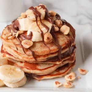 Stack of pancakes topped with banana, chocolate and nuts.