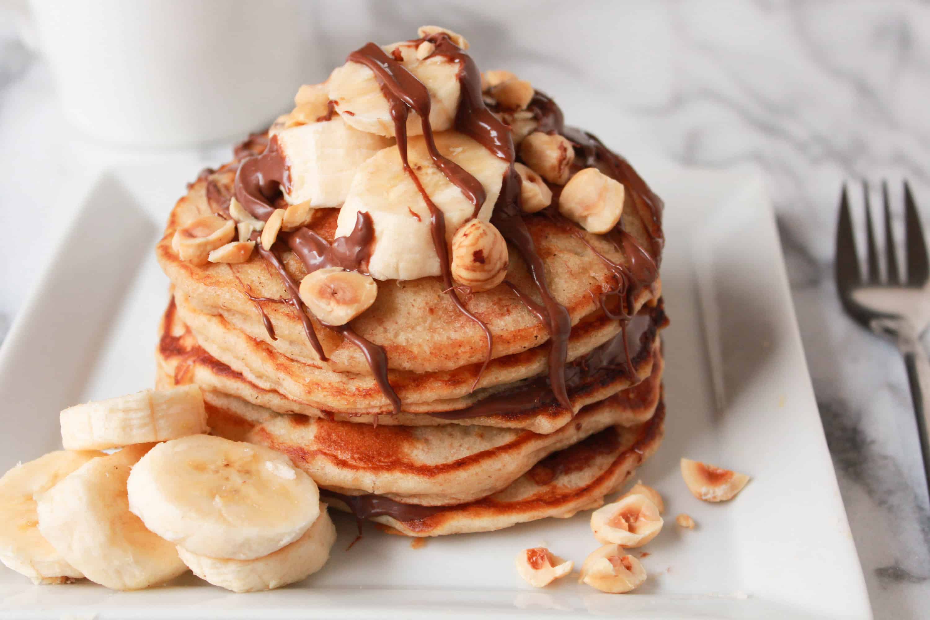 Stack of pancakes topped with banana, chocolate and nuts. 