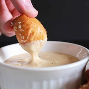 Pretzel bite being dipped into a bowl of cheese sauce.