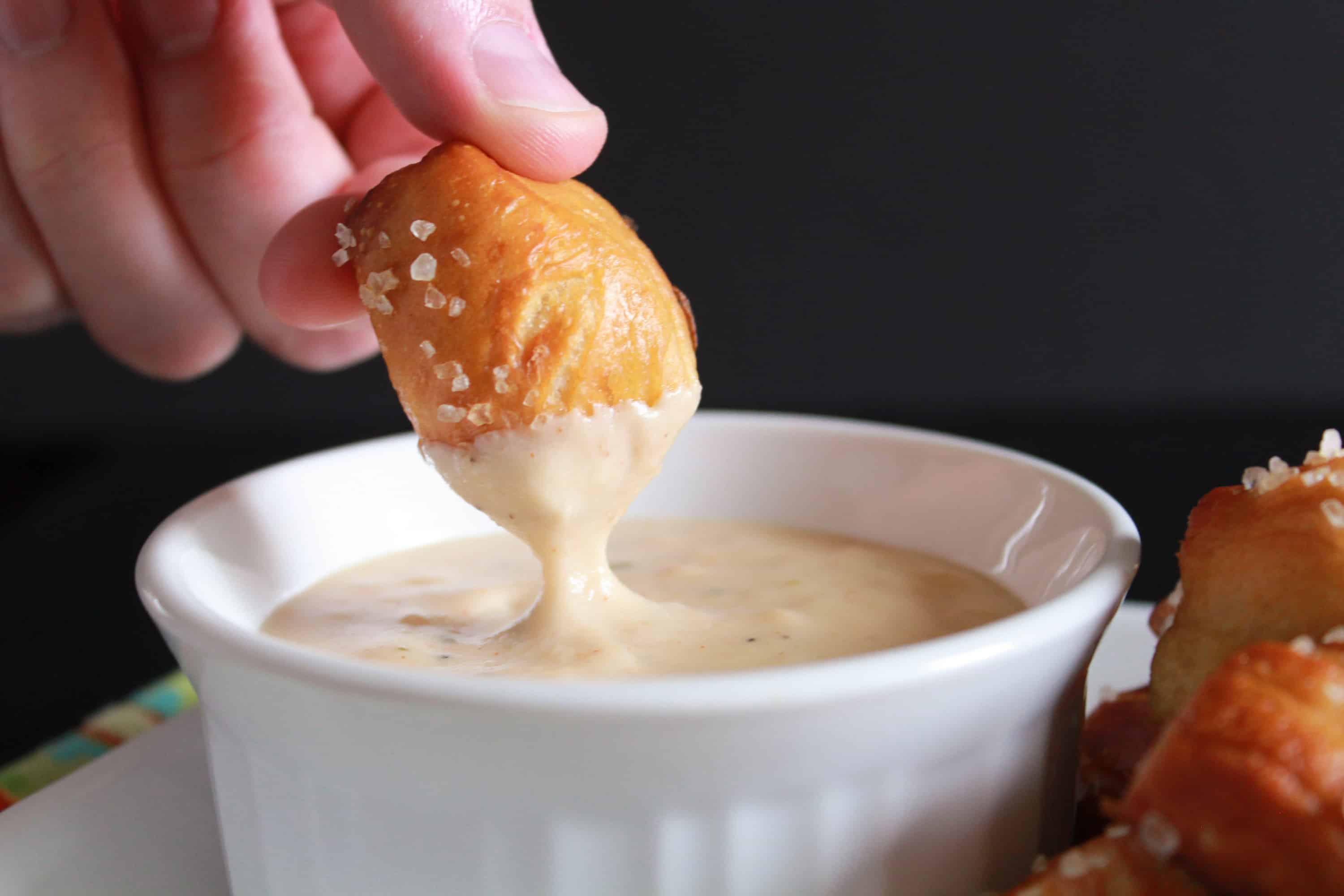 Pretzel bite being dipped into a bowl of cheese sauce. 