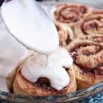 White icing being drizzled onto cinnamon rolls.