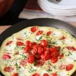 Cooked eggs in a cast iron skillet topped with cherry tomatoes.