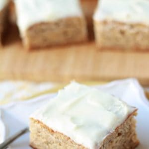 Square slice of cake with white frosting on a white plate.