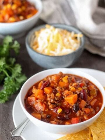 Chili in a white bowl with cheese in the background.