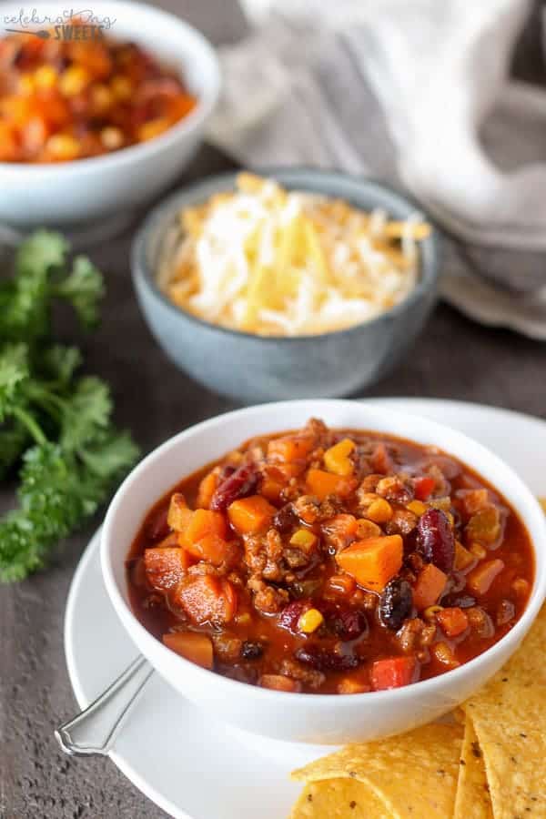 Chili in a white bowl with cheese in the background.