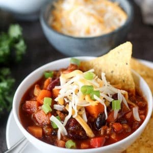 A bowl of chili topped with grated cheese, green onions, and tortilla chips.
