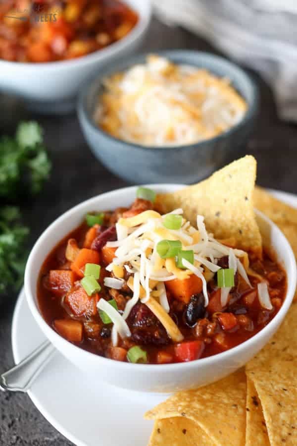 A bowl of chili topped with grated cheese, green onions, and tortilla chips.