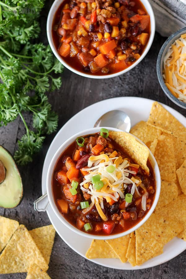 Two bowls of chili with tortilla chips and avocado.