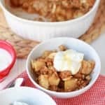 Apple crisp in a white bowl topped with yogurt.
