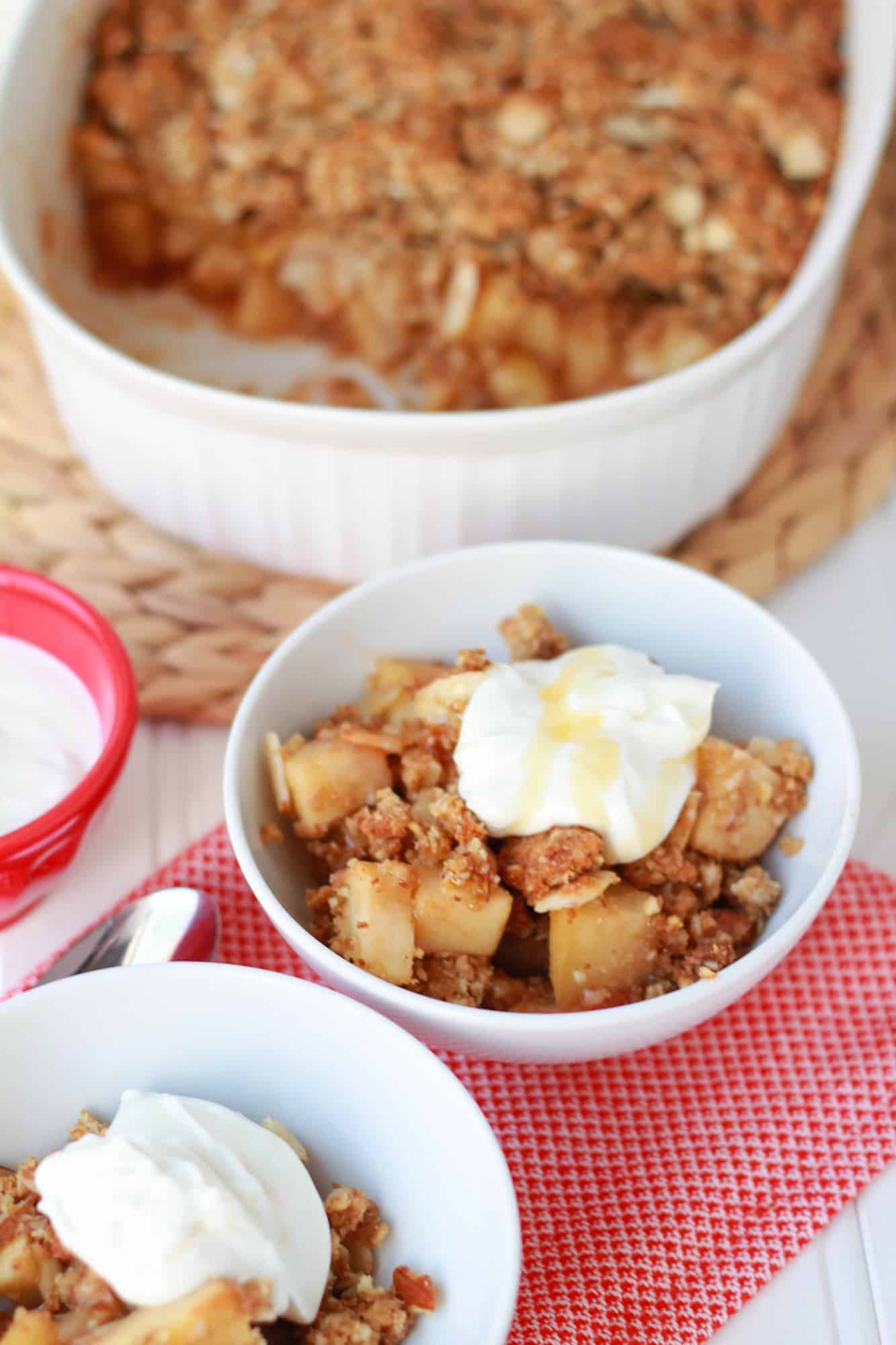 Apple crisp in a white bowl topped with yogurt.