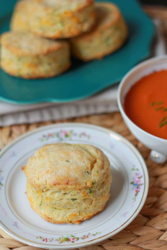 Biscuit on a plate with tomato soup in the background.