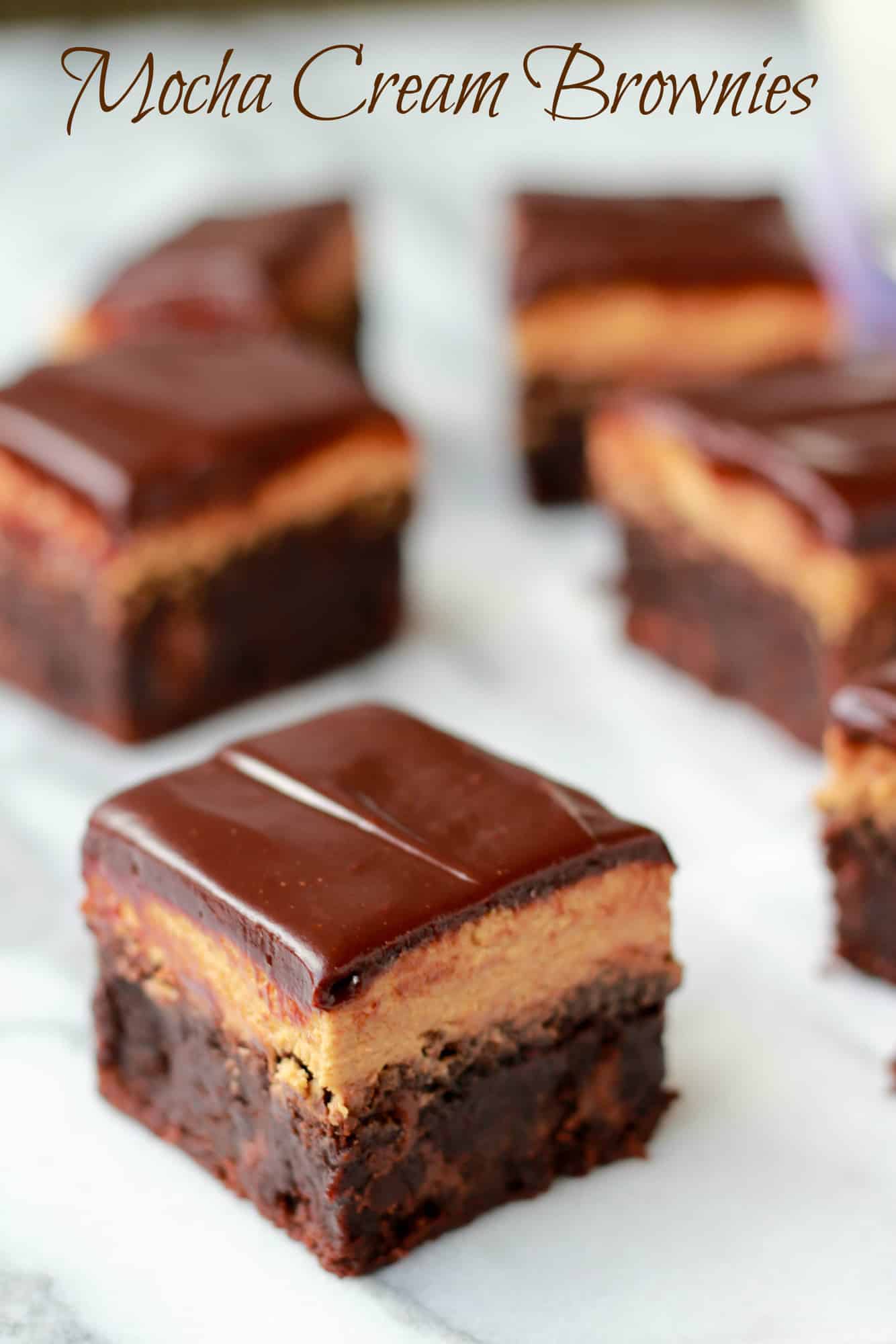 Brownies topped with chocolate frosting on a marble board. 