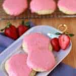 Sugar cookies covered with pink frosting on a purple plate.