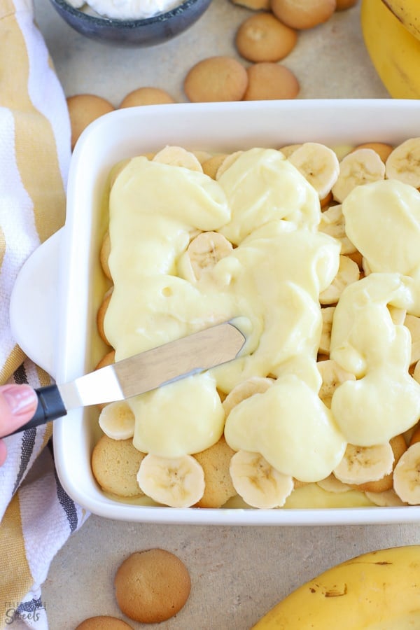 Spreading pudding over layers of banana and cookies.