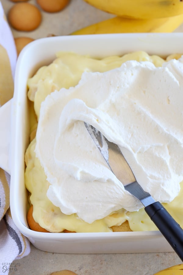 Spreading whipped cream over layers of pudding, cookies and banana. 