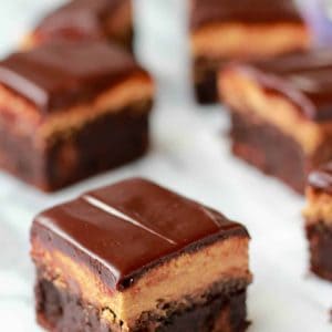 Brownies topped with chocolate frosting on a marble board.