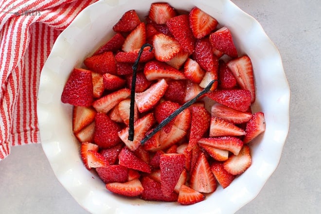 Strawberries, sugar and vanilla bean in a baking dish.