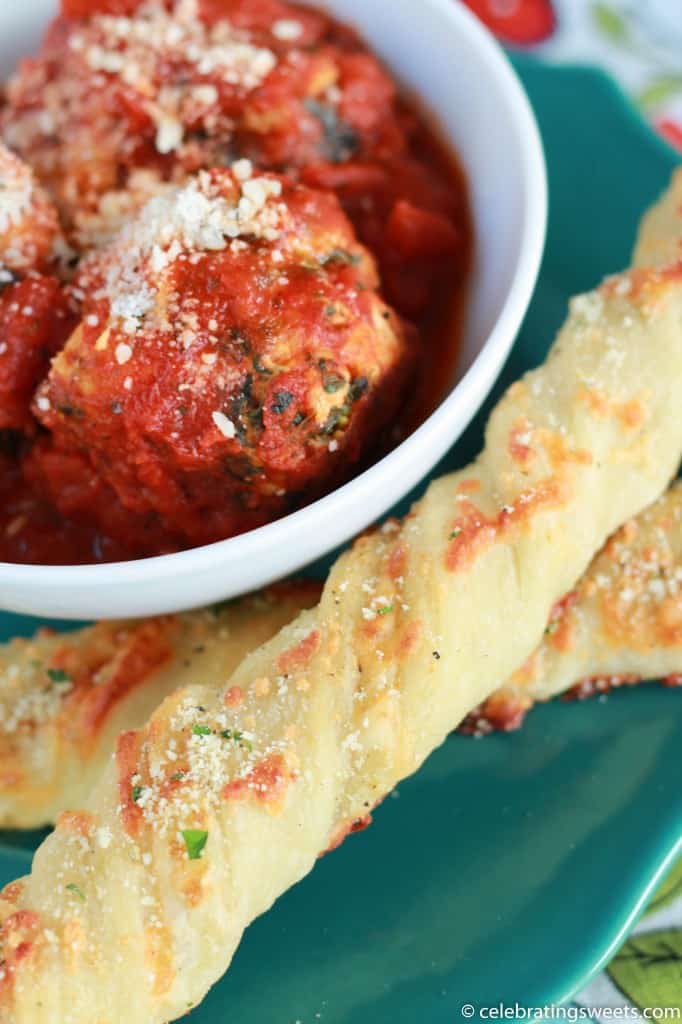 Twisted breadsticks and meatballs on a green plate.