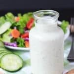 Salad dressing in a glass container with a salad in the background.