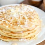 Stack of coconut pancakes topped with coconut syrup, shredded coconut and macadamia nuts.