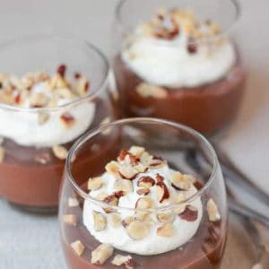 Three glasses filled with pudding topped with whipped cream and nuts.