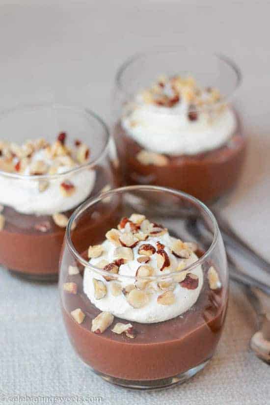 Three glasses filled with pudding topped with whipped cream and nuts.
