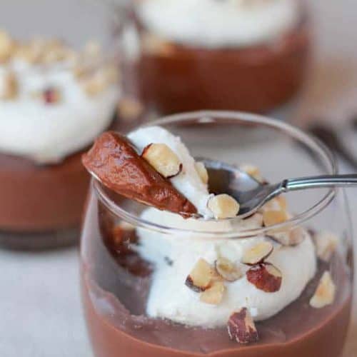 Glass filled with pudding and whipped cream and garnished with nuts.