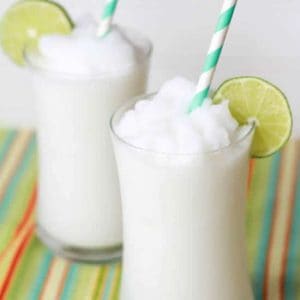 Two glasses filled with a coconut slushie garnished with lime.