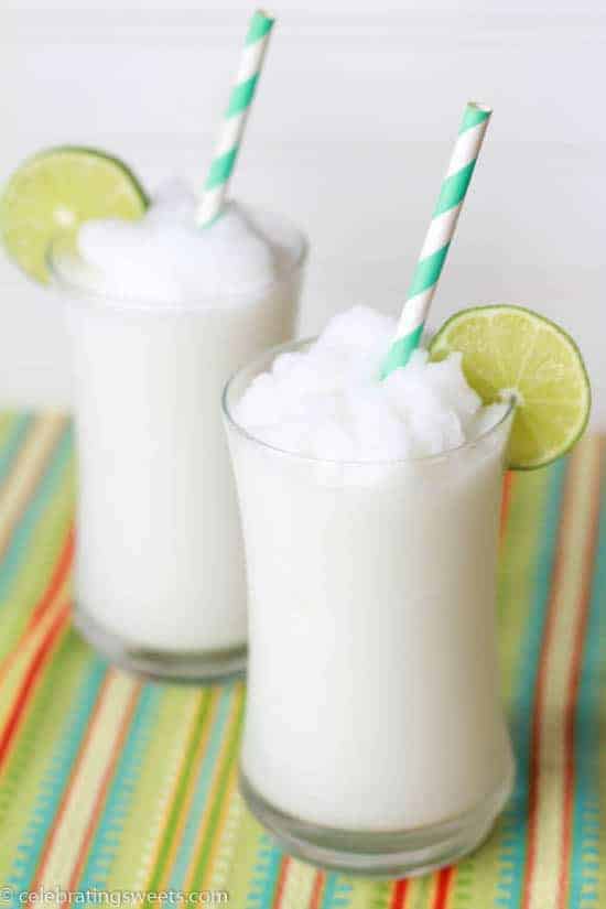 Two glasses filled with a coconut slushie garnished with lime. 