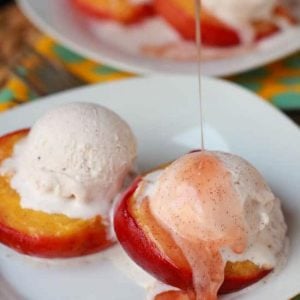 White plate with roasted peaches topped with vanilla ice cream.