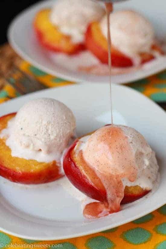 White plate with roasted peaches topped with vanilla ice cream.