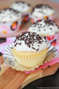 Vanilla cupcake with white frosting and chocolate sprinkles on a wooden board.