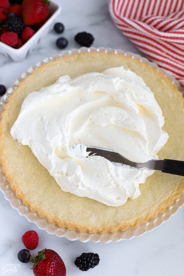 Whipped cream frosting being spread onto a sugar cookie crust.