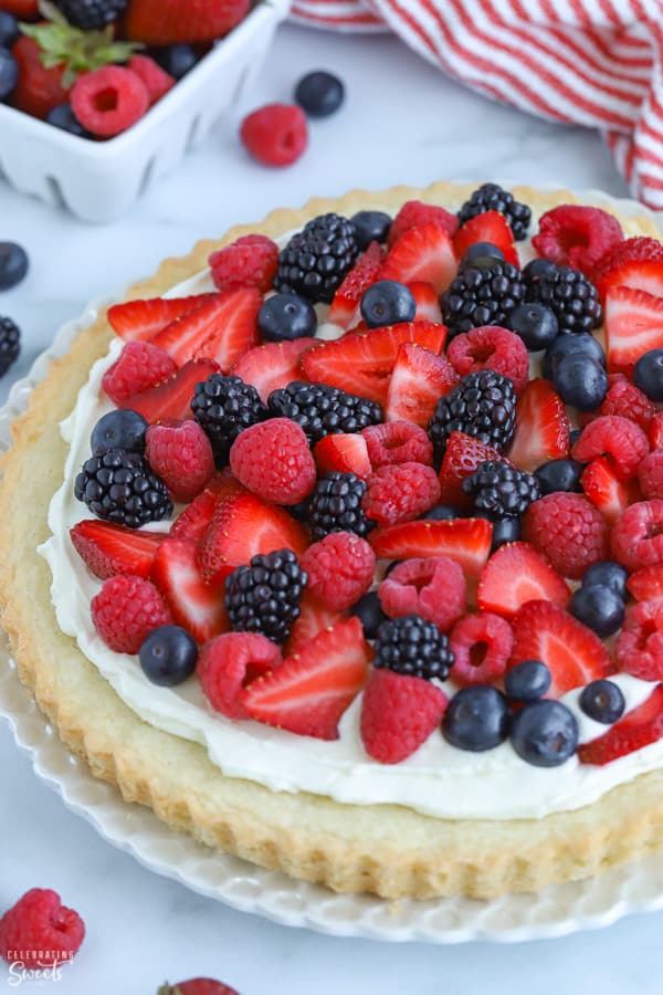 Fruit tart topped with red and blue berries on a white plate.