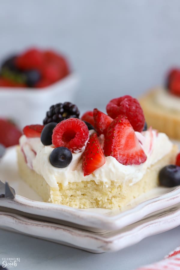 Slice of fruit tart on a white plate topped topped with berries. 