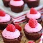 Brownie bites topped with pink frosting and raspberries.