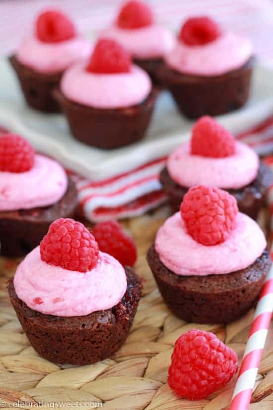 Brownie bites topped with pink frosting and raspberries. 