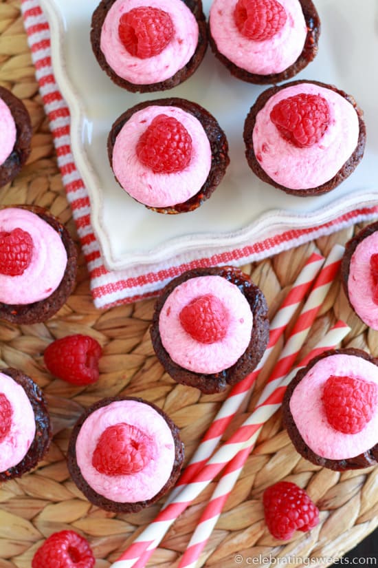 Brownie bites topped with pink frosting and raspberries.