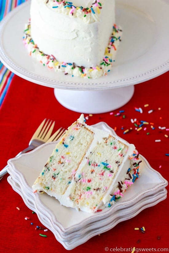 Slice of vanilla cake with colored sprinkles on a white plate.