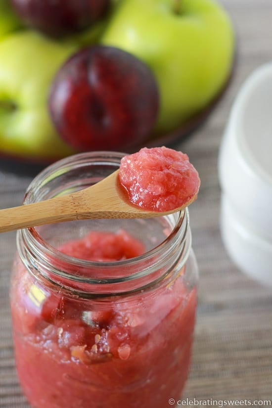 Pink applesauce in a glass jar with a wooden spoon.