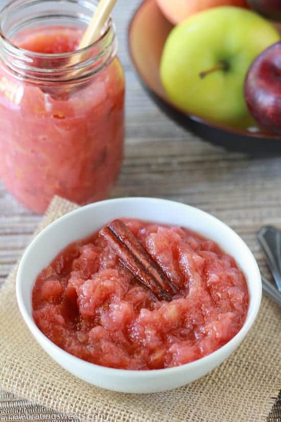 Pink applesauce in a white bowl with a cinnamon stick. 