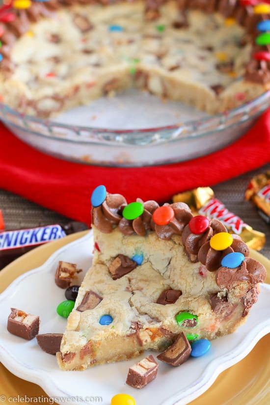 Slice of cookie cake filled with candy bars and topped with chocolate frosting.