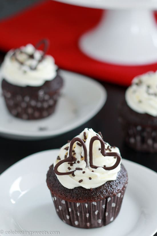 Chocolate cupcakes topped with vanilla frosting and chocolate sprinkles on a white plates.