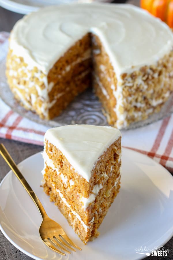 A slice of carrot cake on a white plate with a gold fork.