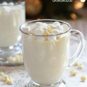 A close up of a glass cup on a table filled with white hot chocolate.