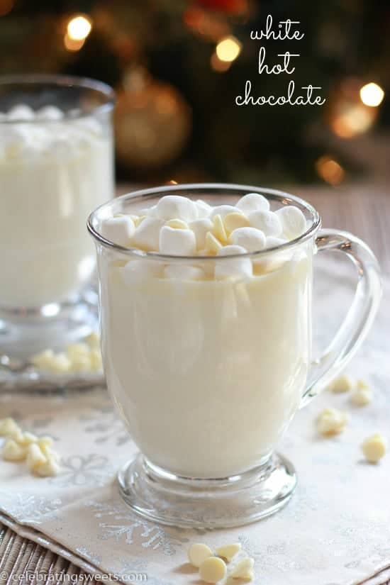 A close up of a glass cup on a table filled with white hot chocolate.